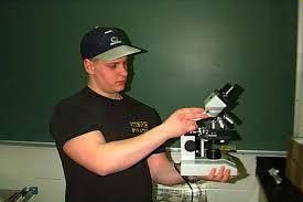 Why do you place one hand under the base of the microscope as you carry it?
